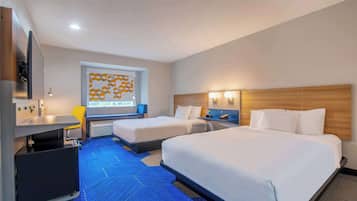 Ein Hotelzimmer mit zwei Betten, einem Schreibtisch, einem Stuhl, einem Fernseher und einem Fenster mit einem geometrischen Muster.