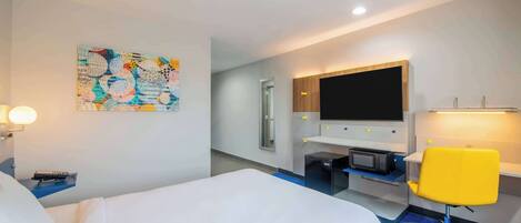 Une chambre d’hôtel comprenant un lit, un bureau avec un ordinateur, une chaise, un téléviseur et une œuvre d’art murale.