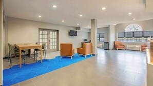 A spacious lobby with a blue carpet, a wooden table with chairs, orange seating, a TV mounted on the wall, and a large arched window with a view. - Microtel Inn & Suites by Wyndham Anderson/Clemson (Anderson)