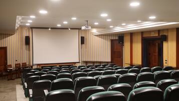 Une salle de conférence avec des rangées de chaises, un écran de projection et un tableau blanc.
