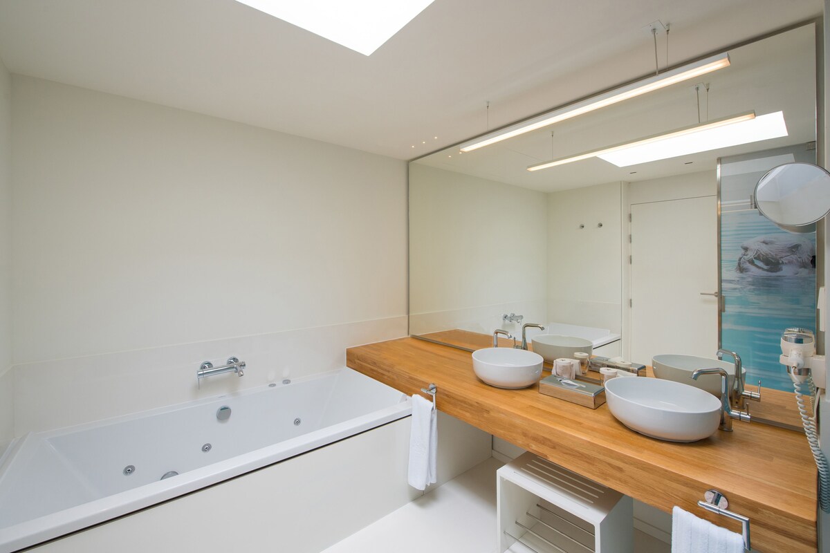 Un baño moderno con una bañera independiente, un tocador de madera con dos lavamanos y un espejo grande.