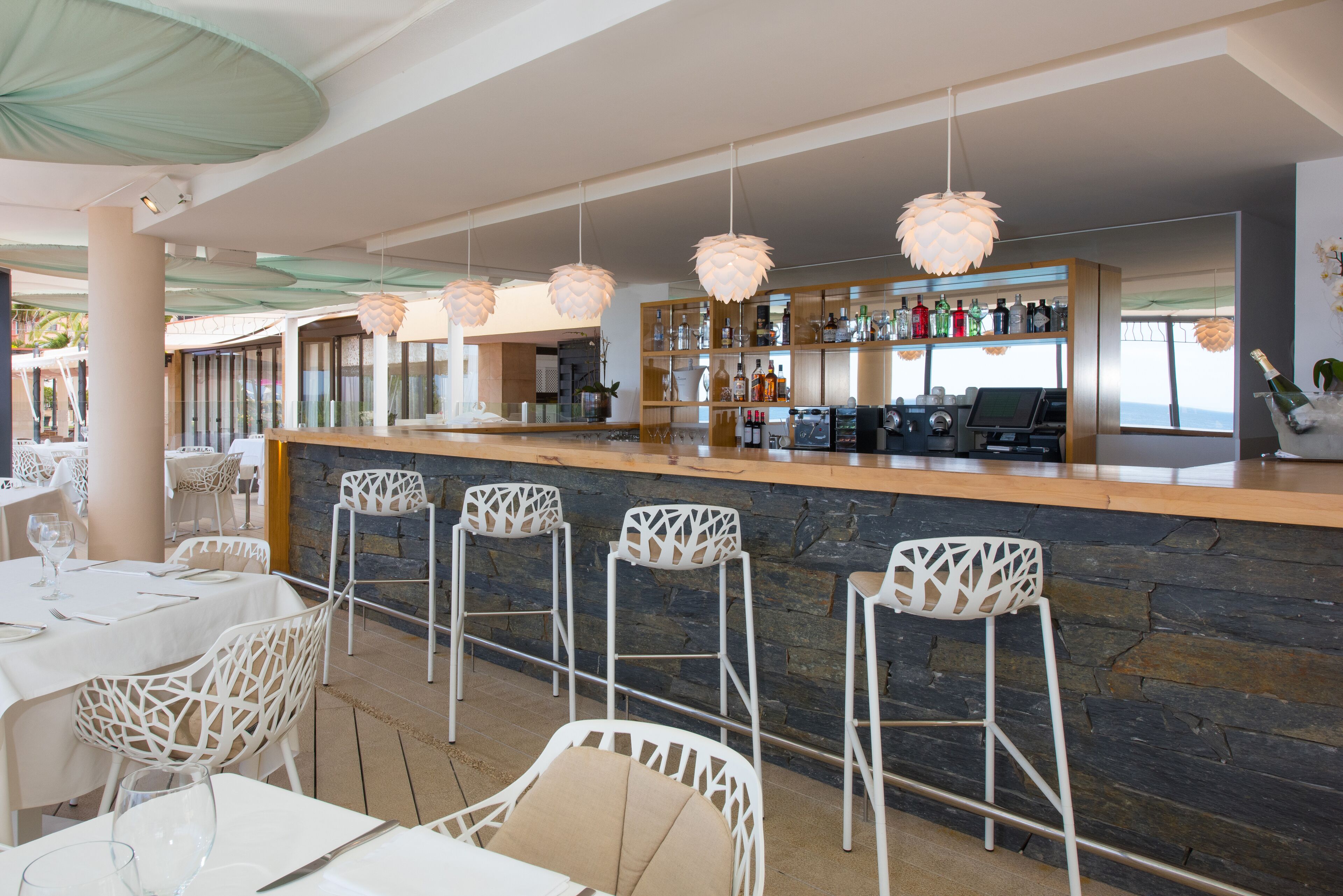 A bar area with white bar stools, a stone counter, and a variety of bottles.