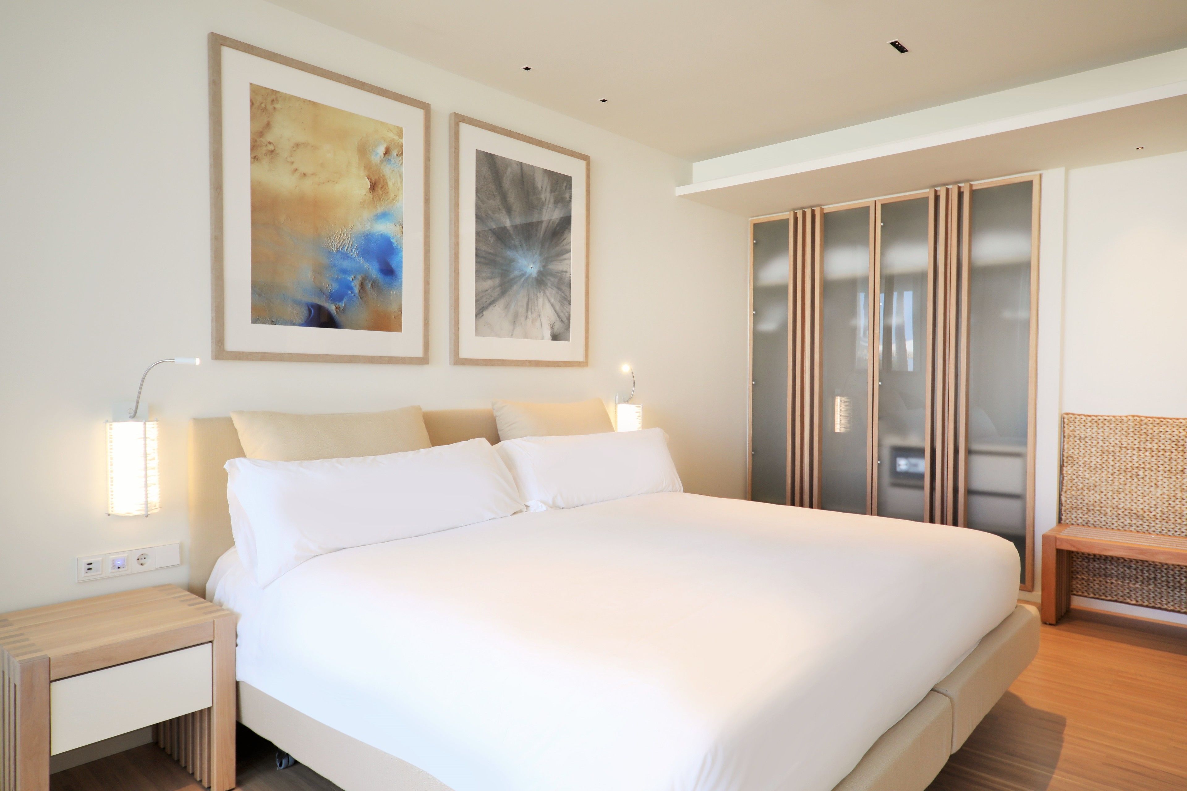 A modern bedroom with a large bed, bedside tables, a wardrobe, and abstract wall art.