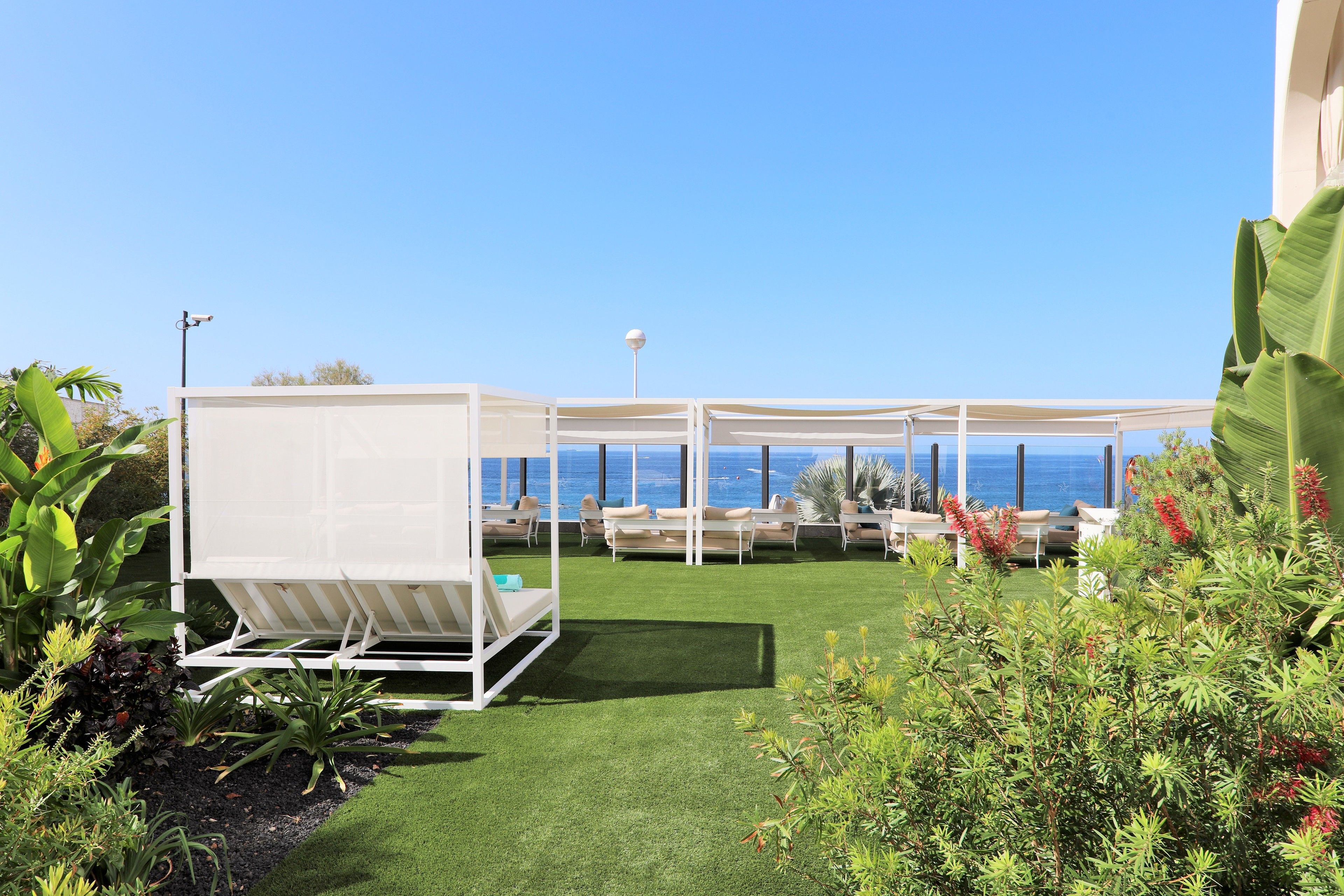 Terraza en la azotea con vistas despejadas al océano, amueblada con sillones blancos y una estructura tipo toldo.