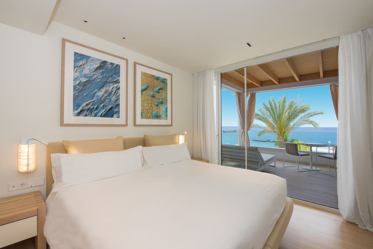 A bedroom with a large bed, a nightstand, and a view of the ocean through a sliding glass door.
