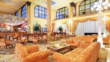 Un hall espacioso con muebles ornamentales, ventanas amplias y un candelabro.