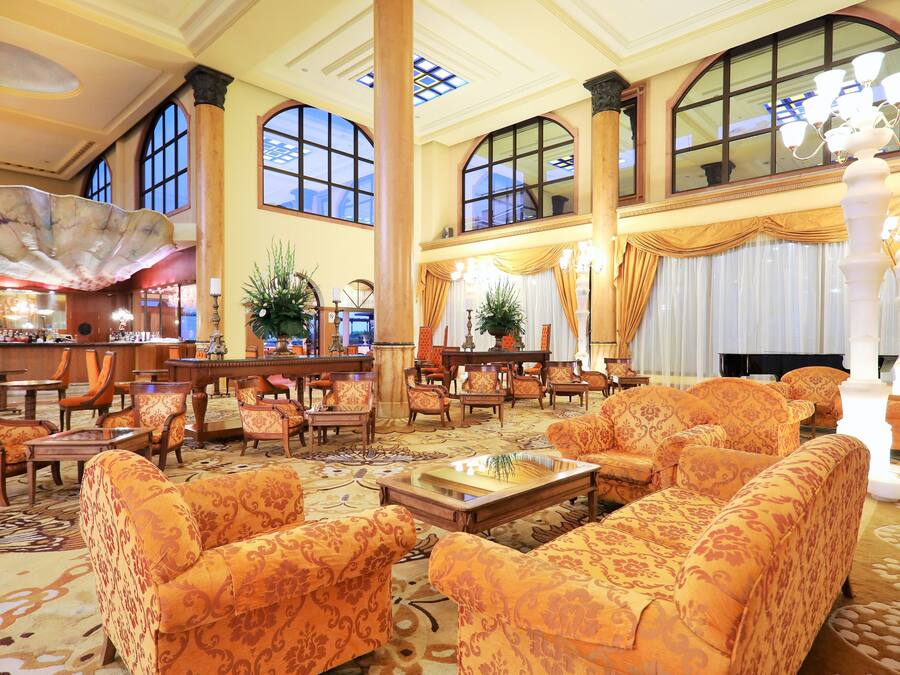 Un hall espacioso con muebles ornamentales, ventanas amplias y un candelabro.