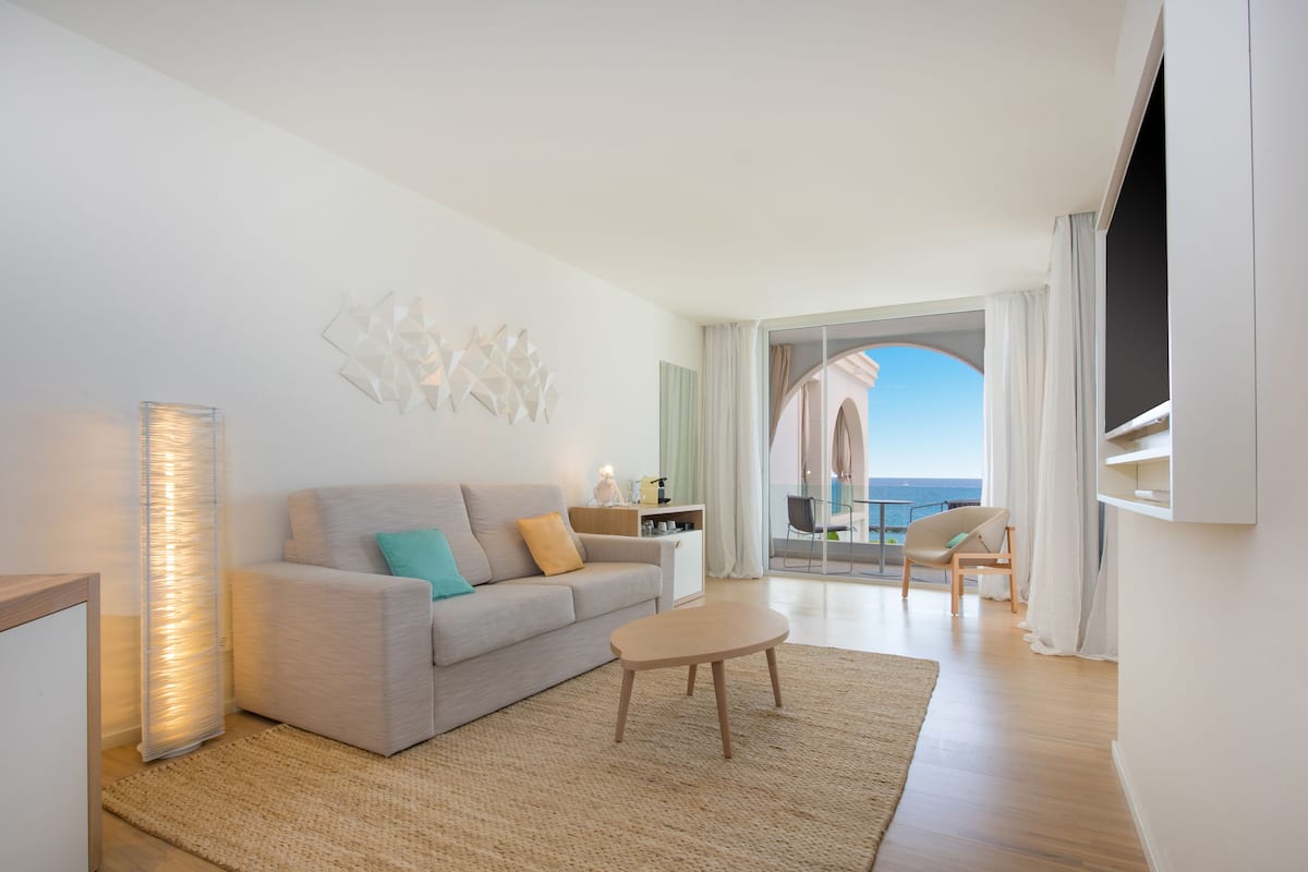 A modern living room with a sofa, coffee table, and a view of the sea through a glass door.