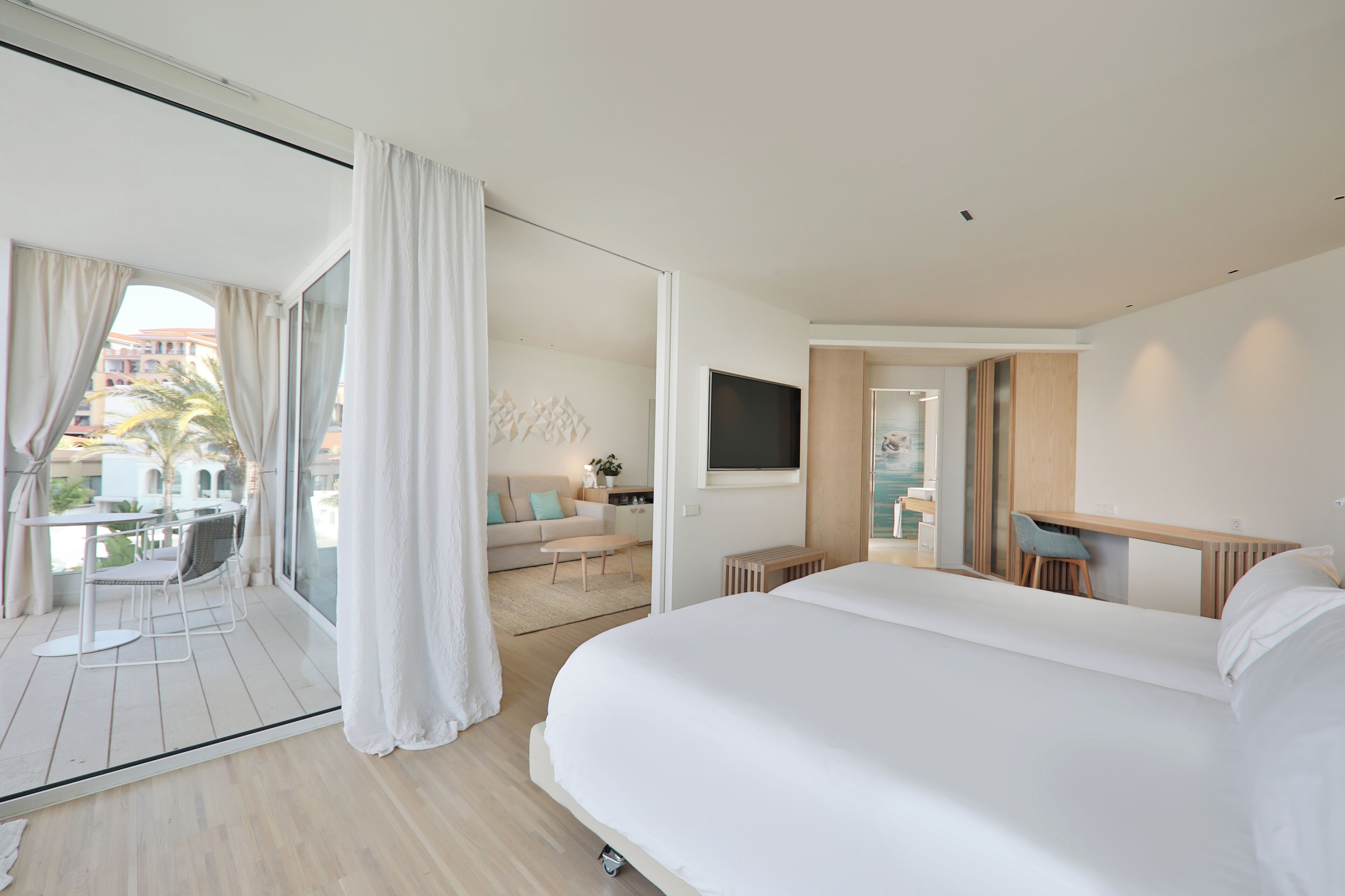 Una habitación de hotel moderna con una cama grande, un escritorio, un televisor y un balcón con cortinas.