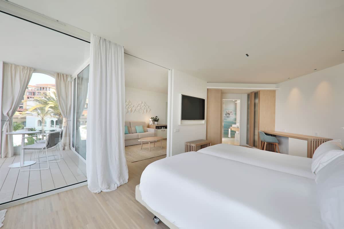 Una habitación de hotel moderna con una cama grande, un escritorio, un televisor y un balcón con cortinas.