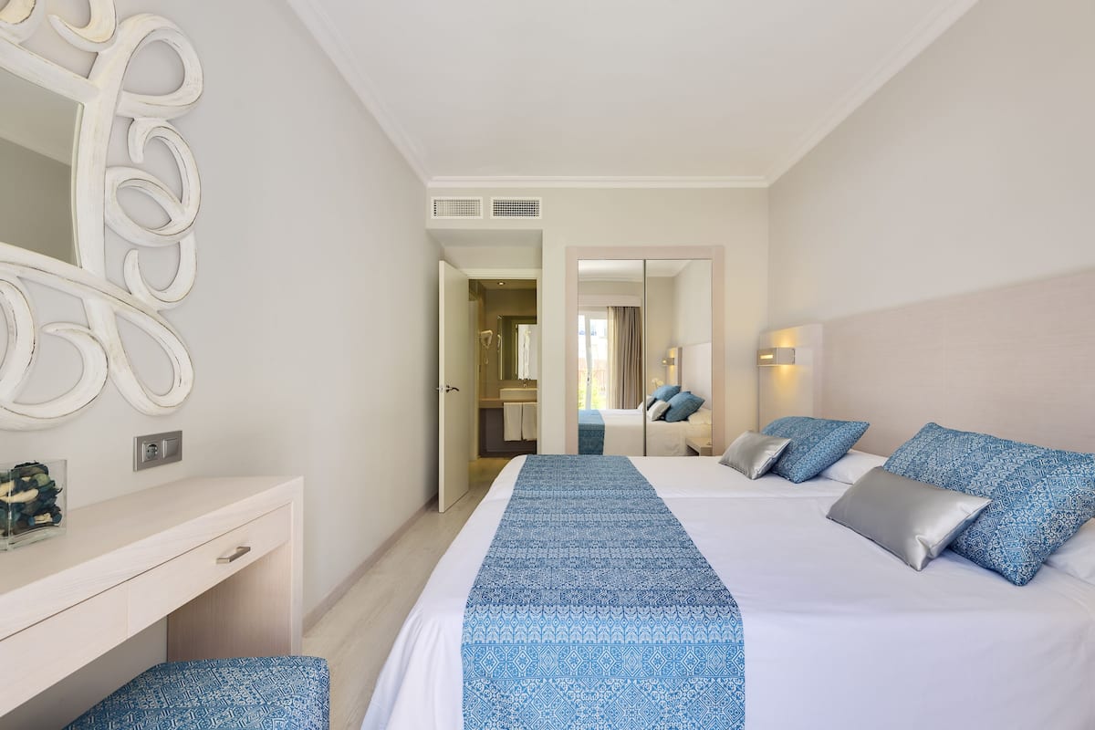 A hotel room with a large bed, a desk, and a mirror.