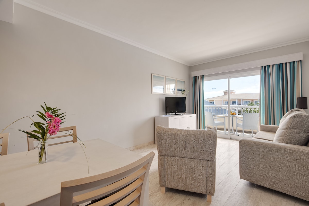A modern hotel room with a dining area, a sofa, and a TV.