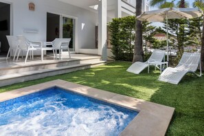 Una piscina con borde de azulejos, rodeada por un césped cuidado y sillones blancos.