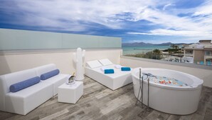 A modern outdoor lounge area with a white sofa, a daybed, and a freestanding bathtub. - Playa Garden Selection Hotel & Spa (Muro)