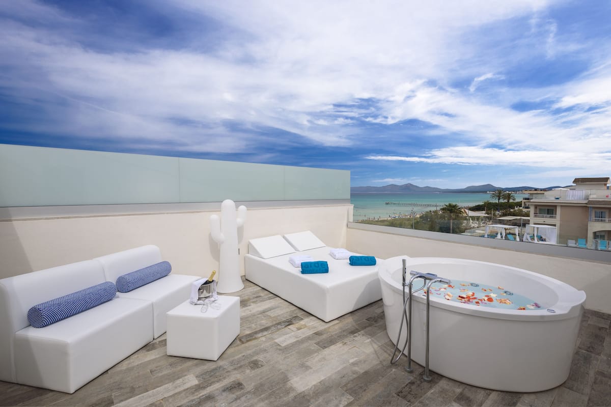 A modern outdoor lounge area with a white sofa, a daybed, and a freestanding bathtub.