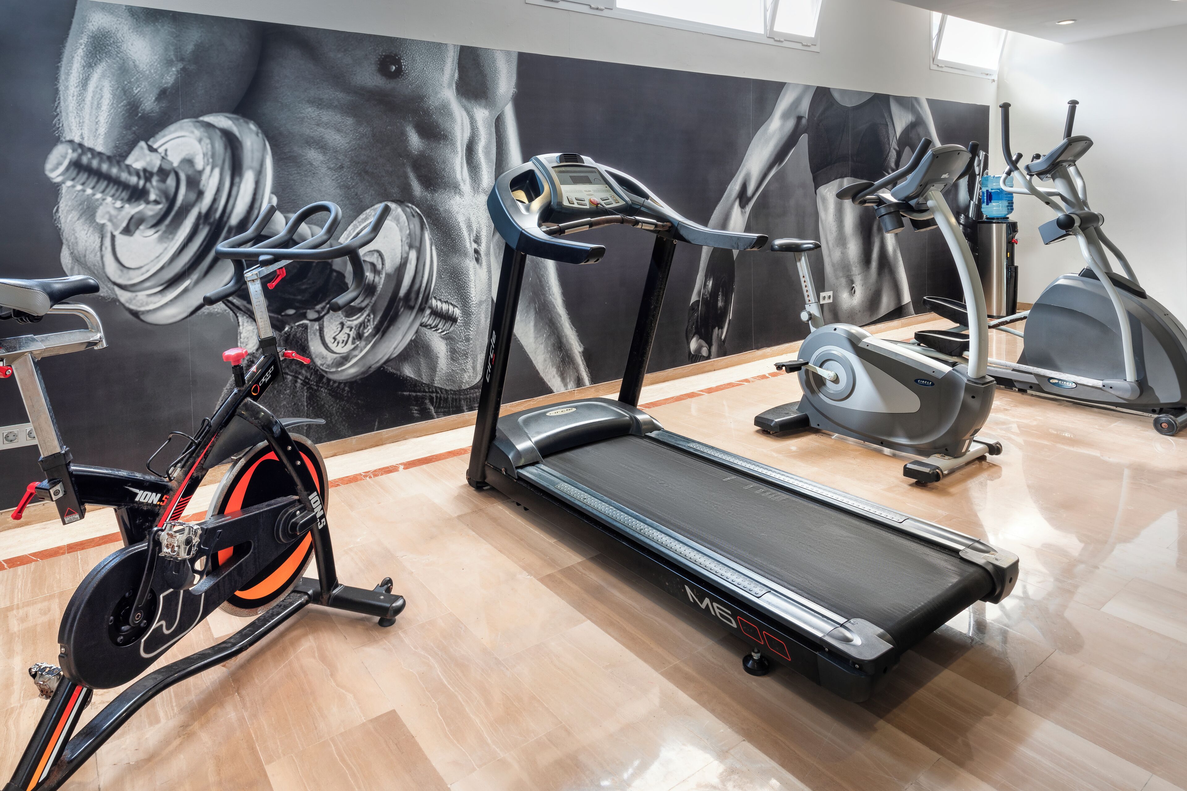A gym with exercise equipment, including a stationary bike, treadmill, and elliptical machine.