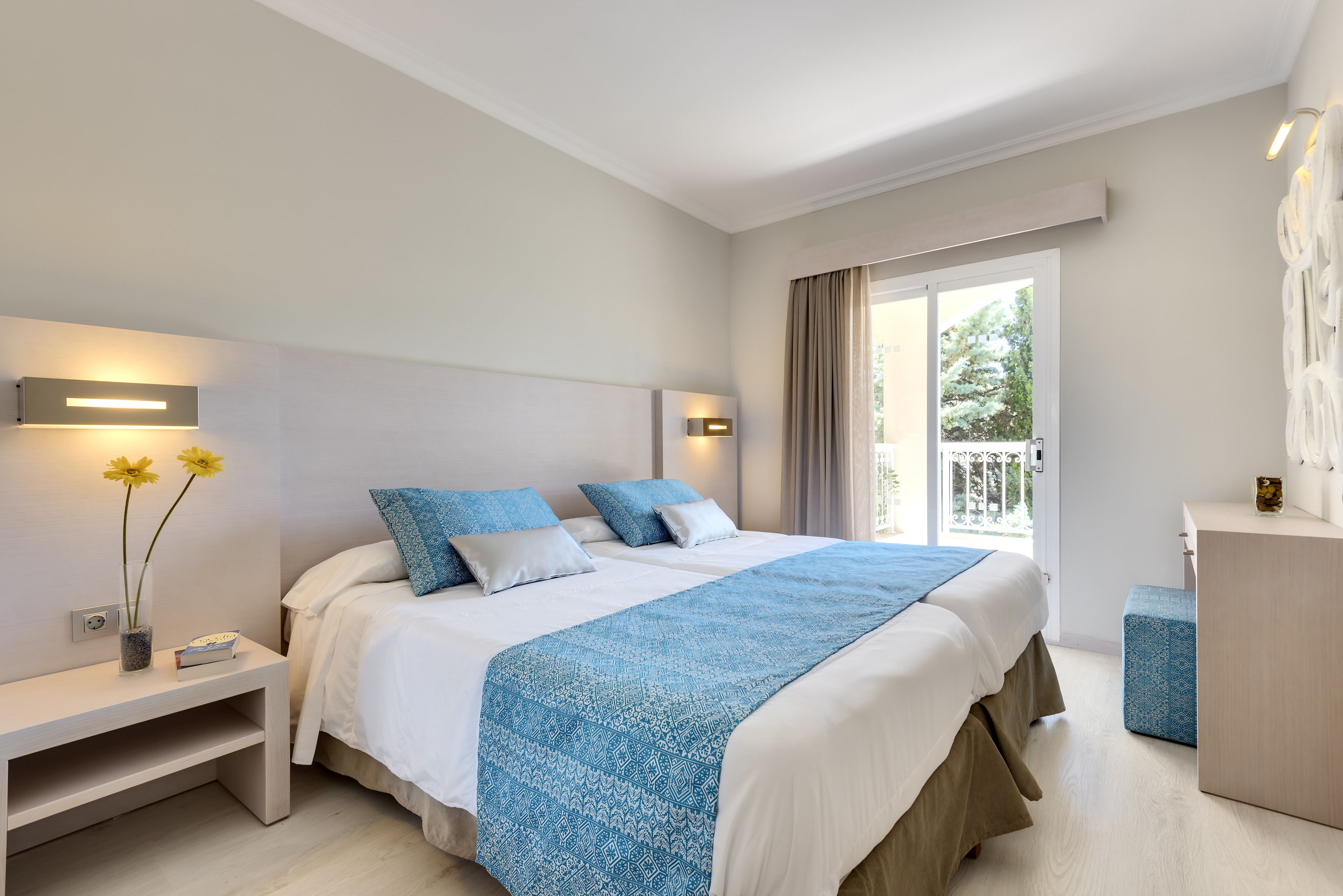 Een hotelkamer met een groot bed, een nachtkastje en uitzicht op de omgeving via een schuifdeur.