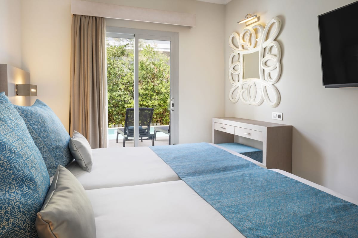 A hotel room with a bed, a desk, a chair, and a large window with a view of greenery.