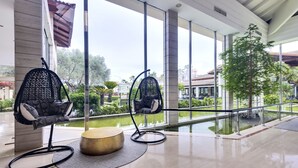 A modern indoor area with two black hanging chairs, a round wooden table, and a view of a water feature and greenery outside. - Playa Garden Selection Hotel & Spa (Muro)