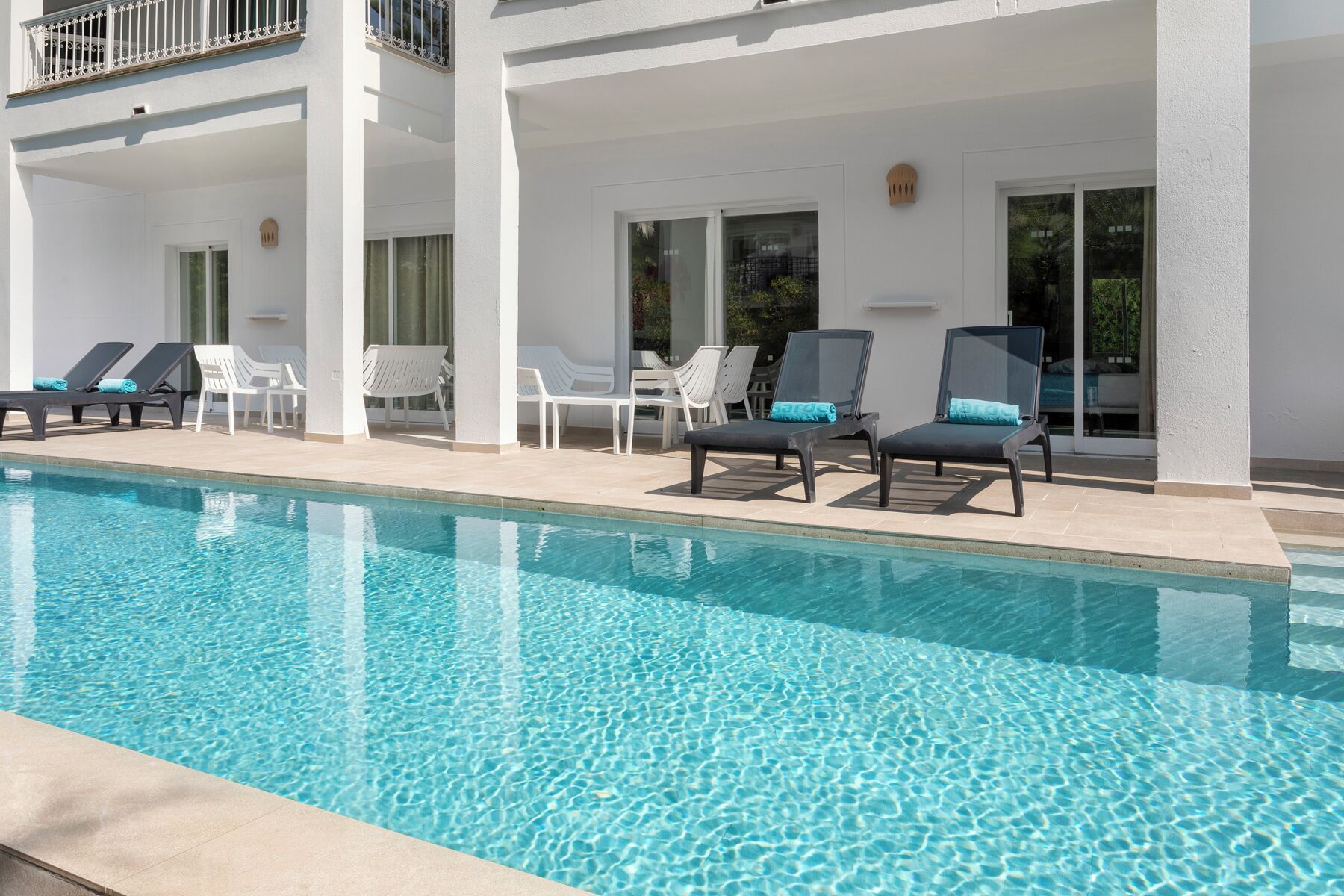 Un área junto a la piscina con sillas de descanso y una piscina cristalina.