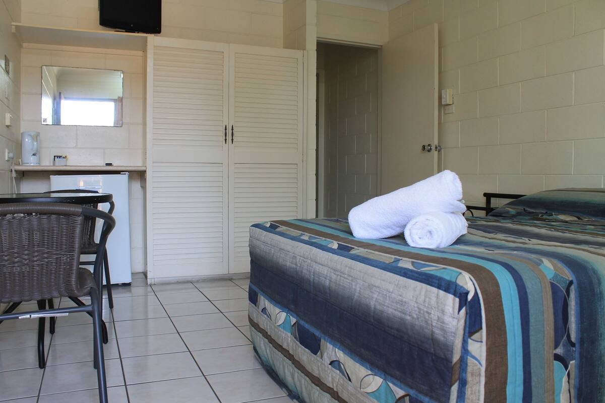 A hotel room with a bed, a chair, a desk, and a wardrobe.