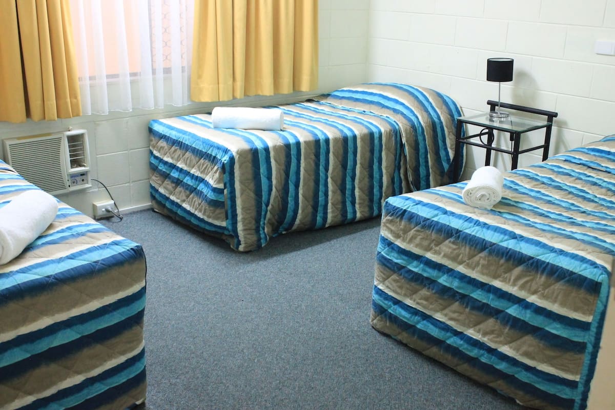 A hotel room with two single beds, a small table with a lamp, and a window with curtains.