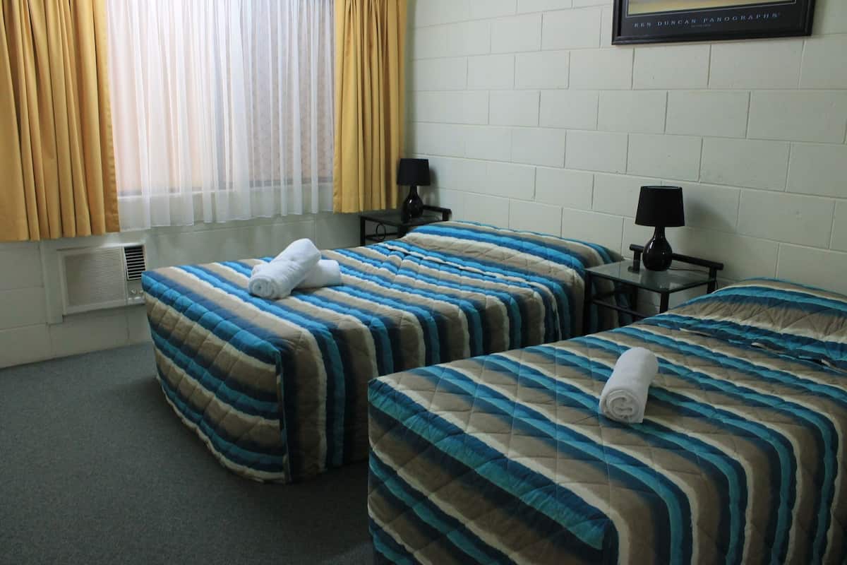 A hotel room with two beds, each with a striped bedspread, two bedside tables with lamps, a framed picture on the wall, and a window with curtains.