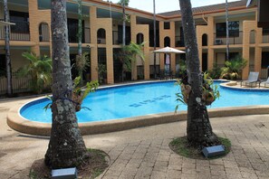 A swimming pool surrounded by trees and a building with balconies. - Oasis Inn Cairns (Cairns North)