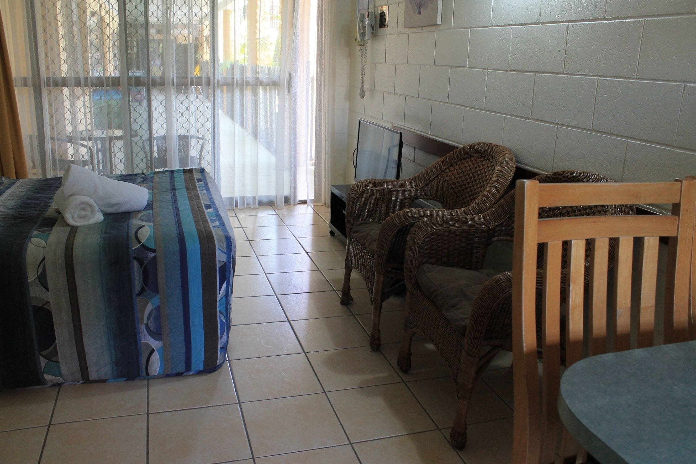 Una habitación con cama, televisión, mobiliario de mimbre y suelo de baldosas.