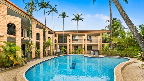 Una piscina rodeada por un edificio con balcones y palmeras.