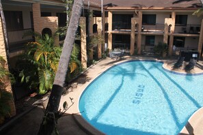A swimming pool with a curved edge, surrounded by a concrete deck. There are lounge chairs and a small table near the pool. - Oasis Inn Cairns (Cairns North)