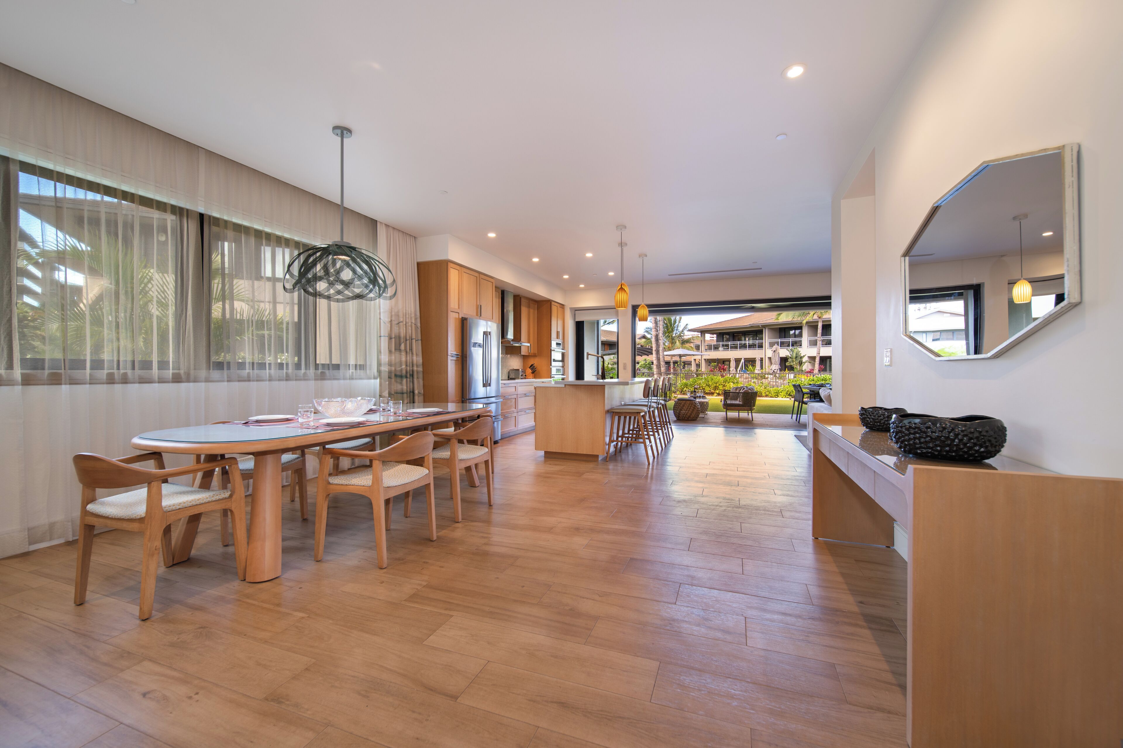 A modern kitchen with wooden cabinets, a central island, and a dining area with a round table and chairs.
