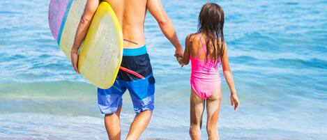 Um homem e uma criança caminham na praia carregando pranchas de surf.