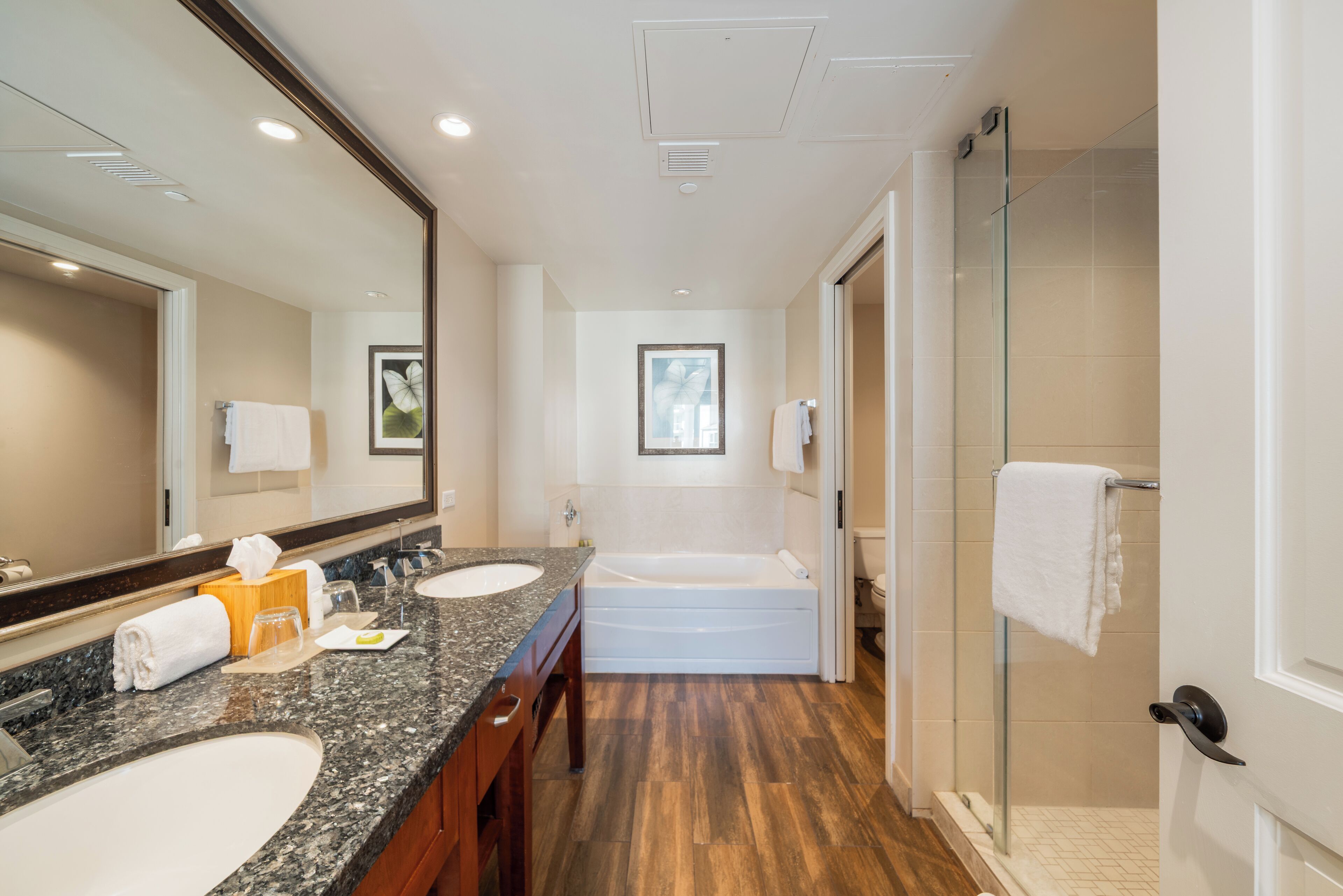 A modern bathroom with a double sink, a large mirror, a bathtub, and a glass shower enclosure.