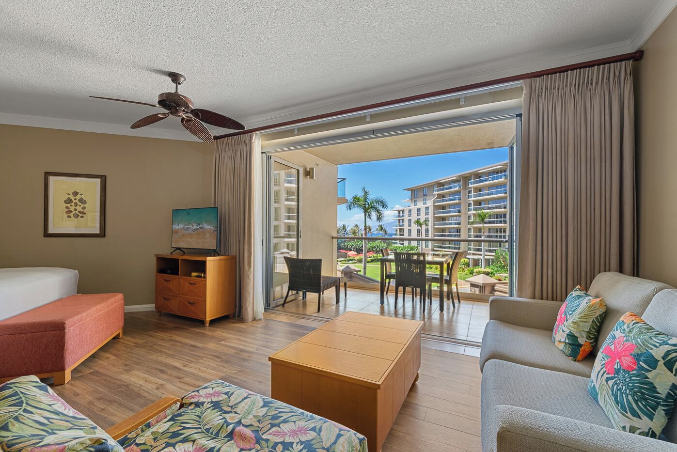 Quarto de hotel com varanda, televisão, sofá, mesa de centro e armário de madeira.