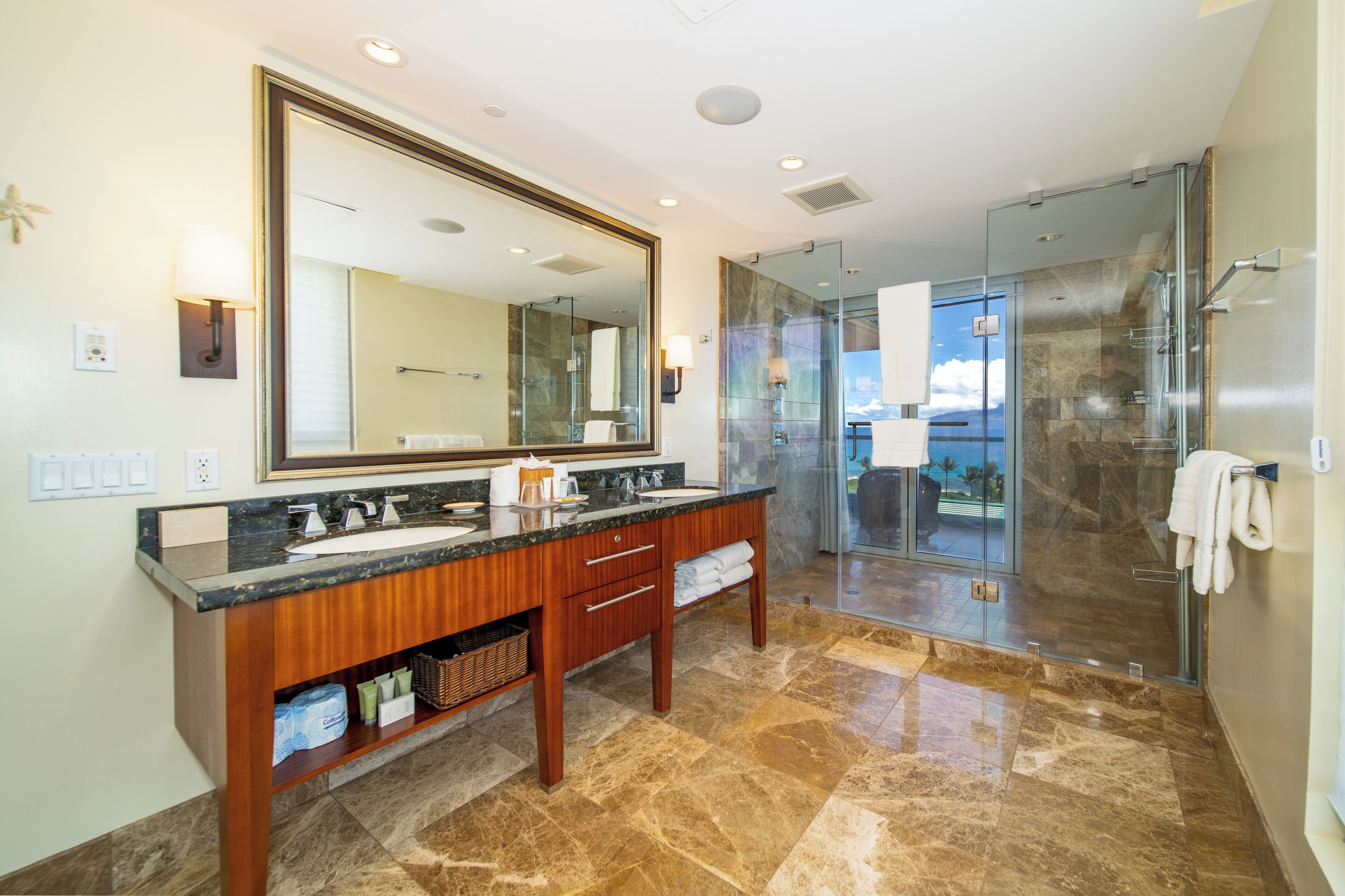 A modern bathroom with a large mirror, dual sinks, and a glass-enclosed shower.