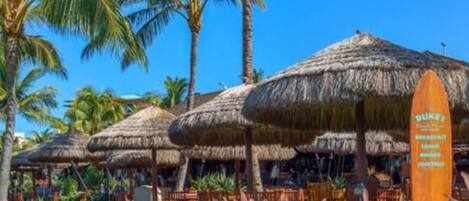 A resort with thatched-roof structures, palm trees, and a surfboard sign.