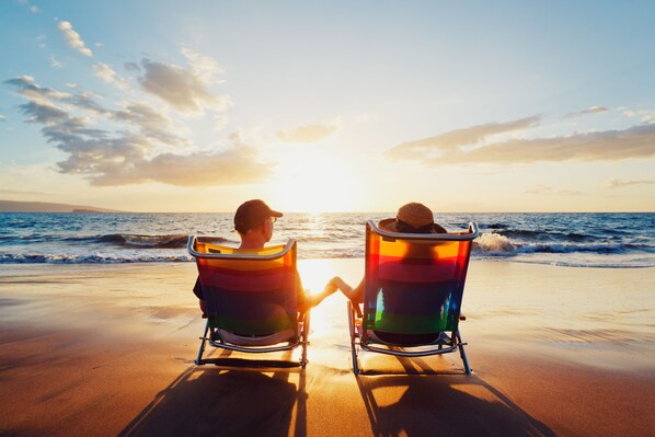 Dos personas sentadas en sillas de playa frente al océano al atardecer.