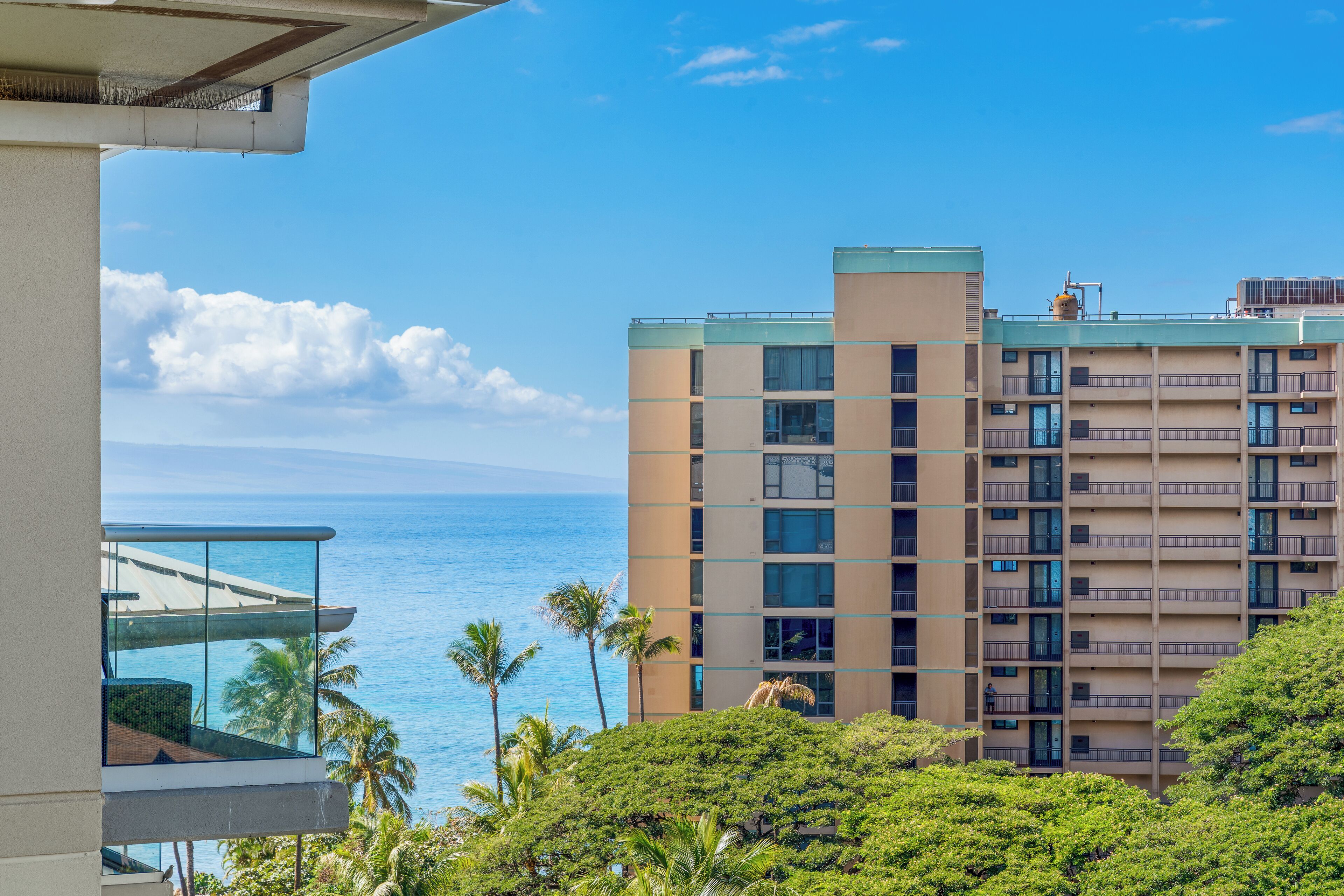 A multi-story building with balconies, a view of the ocean, and palm trees.