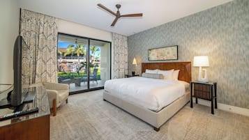 Quarto de hotel com uma cama grande, um ventilador de teto, uma TV e vista para uma palmeira e um prédio pela porta de vidro.
