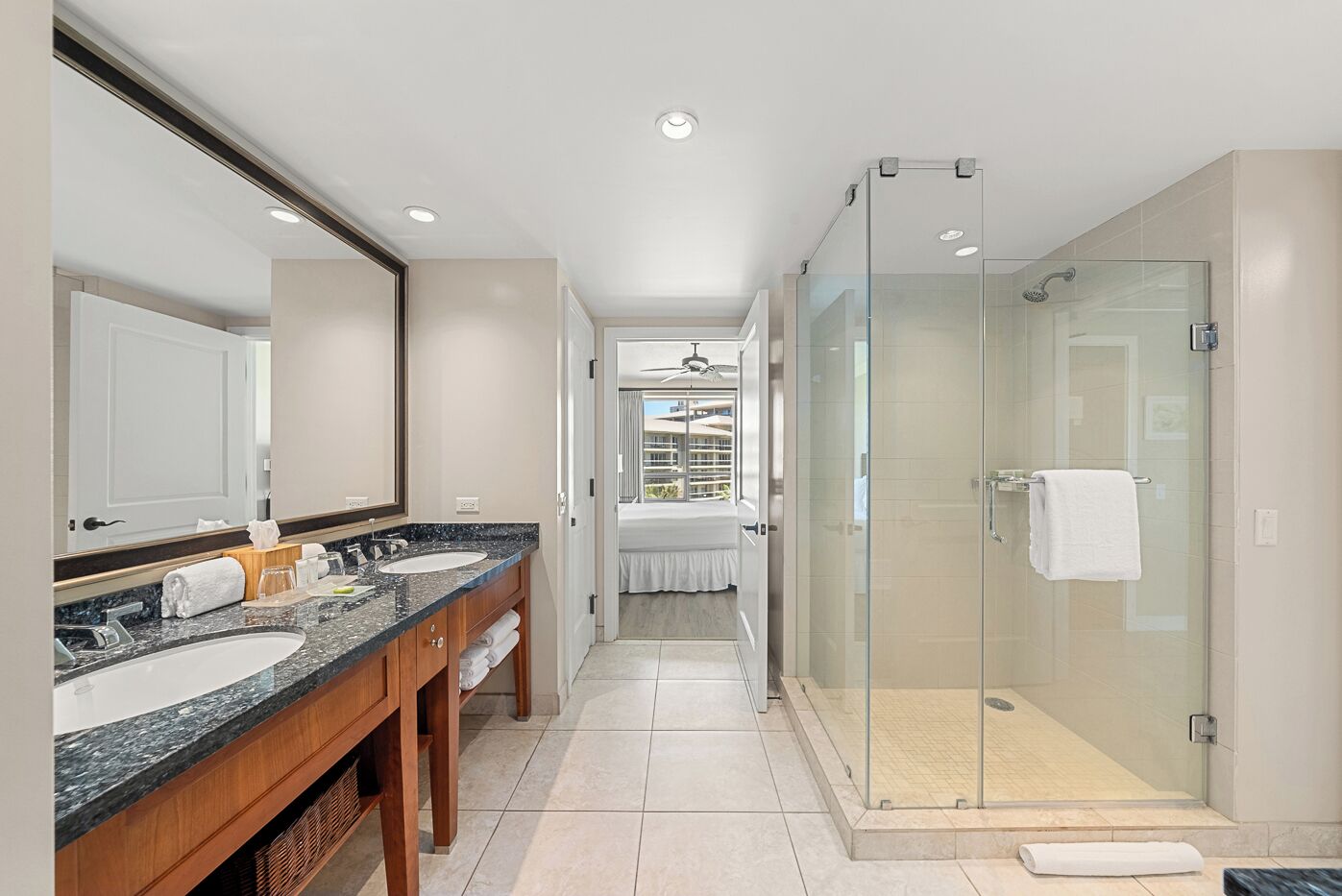A modern bathroom with two sinks, a glass shower enclosure, and a view of a hotel balcony.