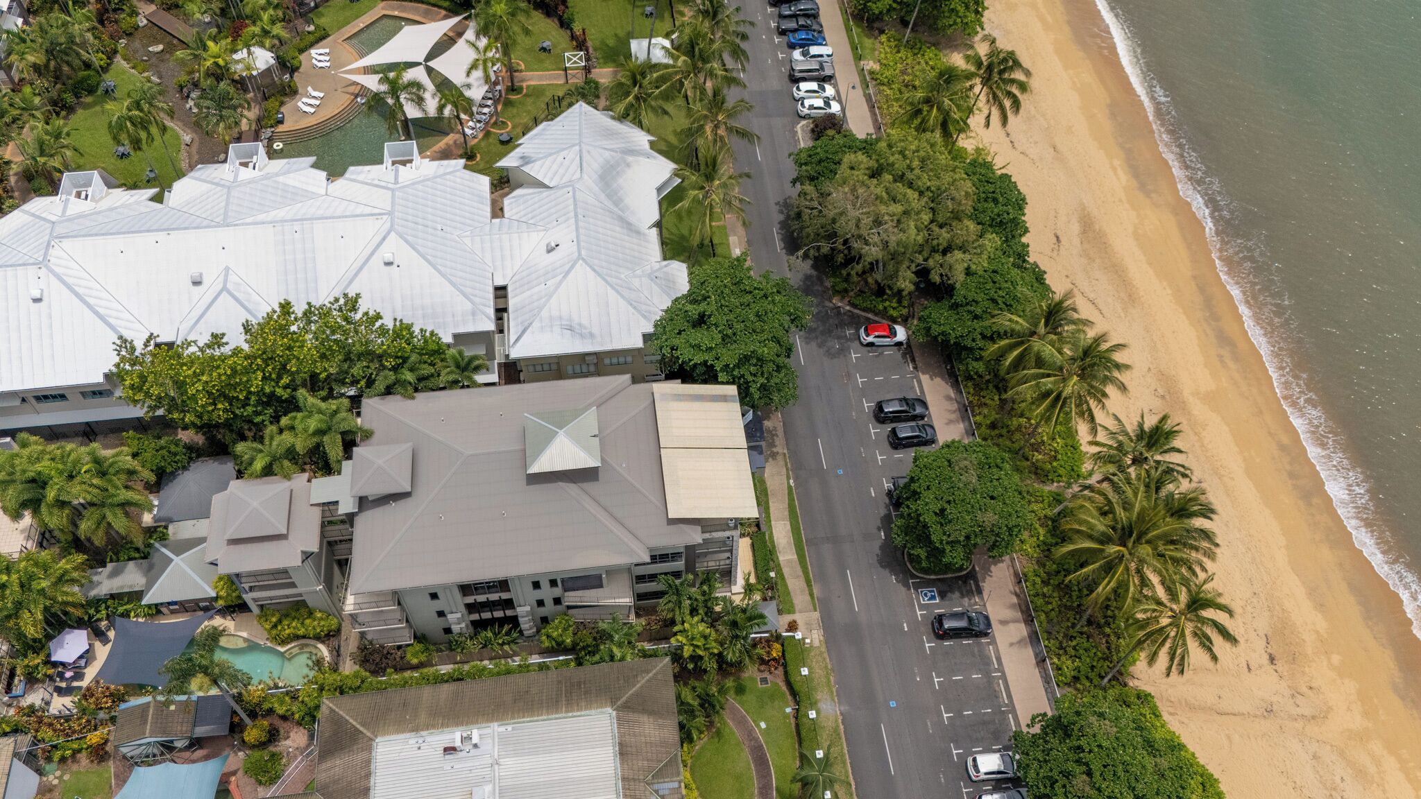 An aerial view of a resort with multiple buildings, a parking lot, and a beach.