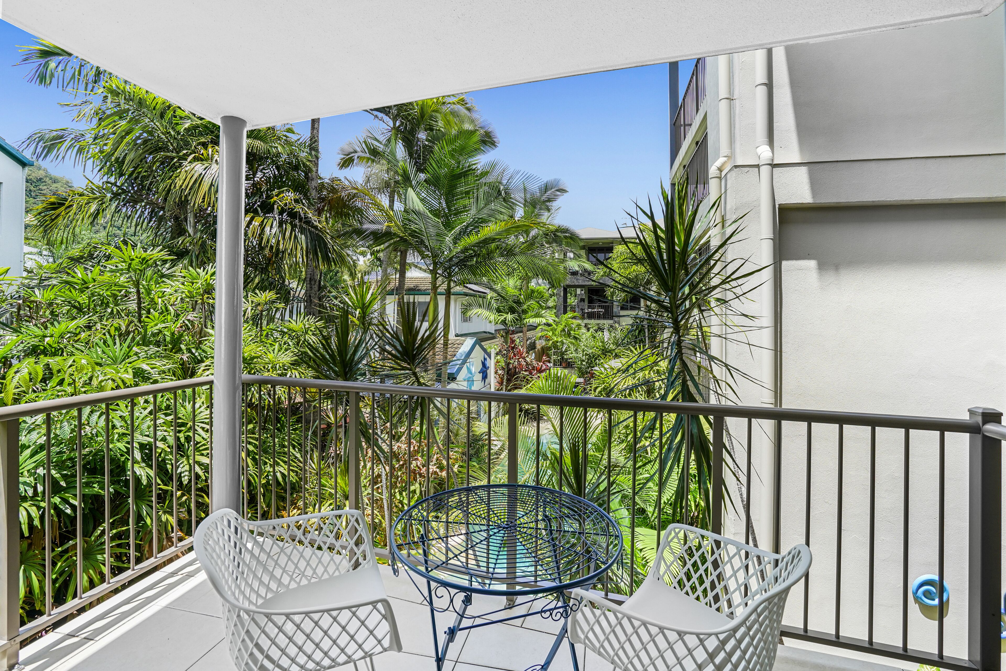 Un balcone con tavolo e sedie, circondato da rigogliosa vegetazione tropicale.