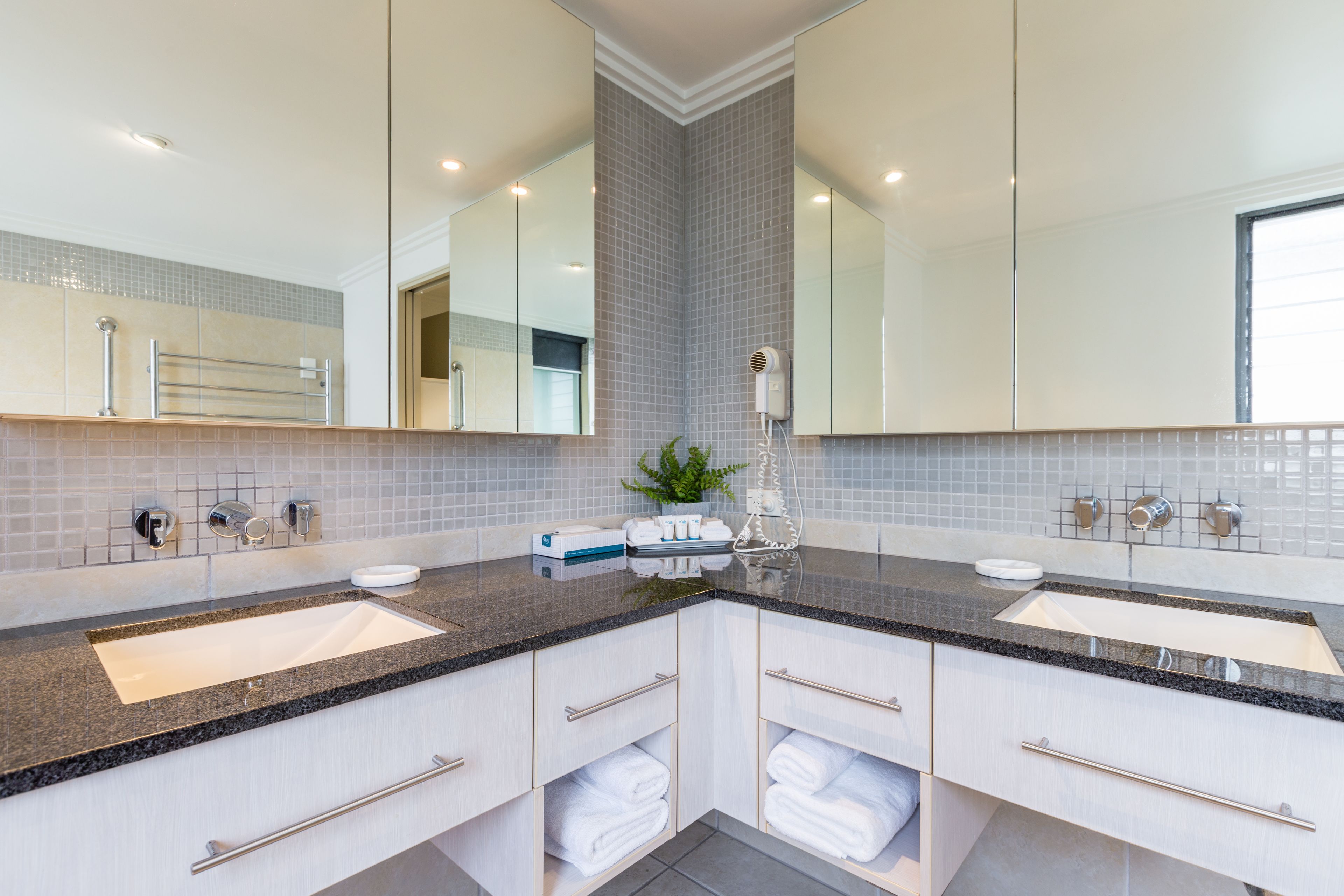 A modern bathroom with two sinks, a large mirror, and a towel rack.