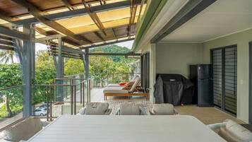 A balcony with a covered seating area, a grill, and a refrigerator.