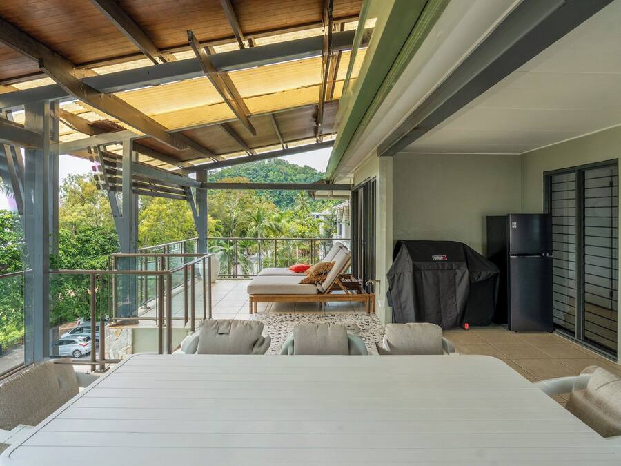 A balcony with a covered seating area, a grill, and a refrigerator.