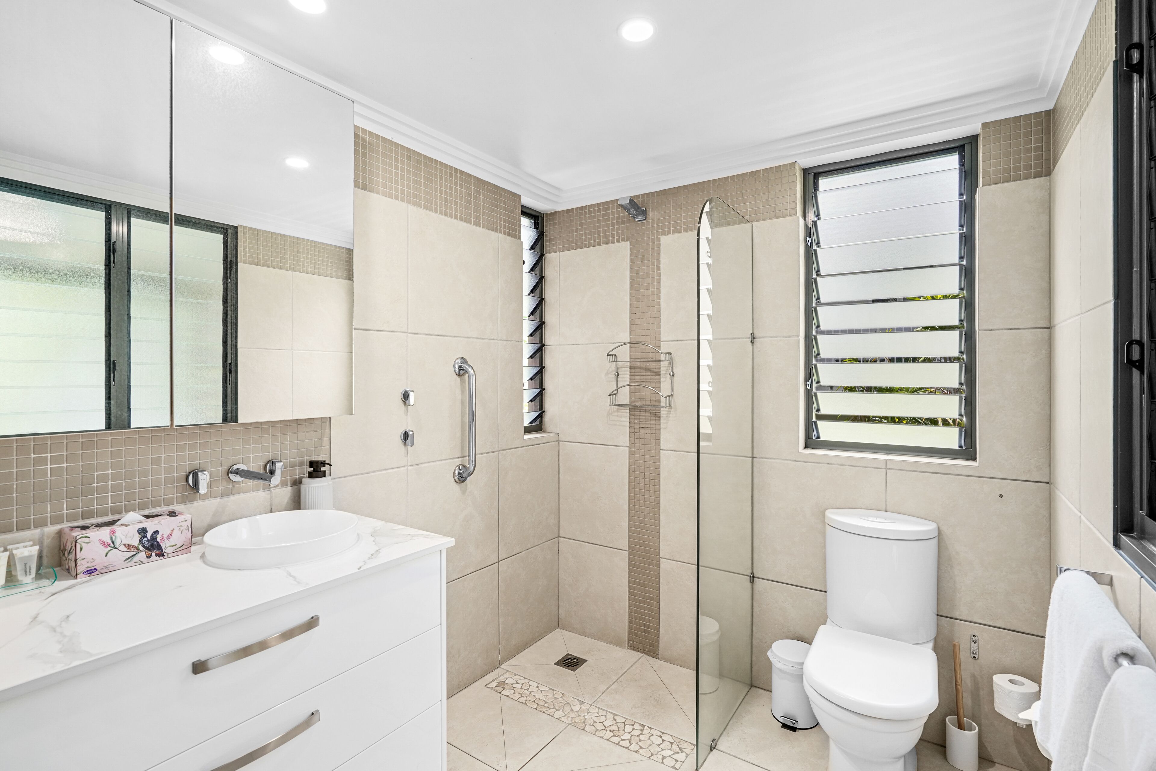 Een moderne badkamer met een douchecabine van glas, een witte wastafel en een toilet.