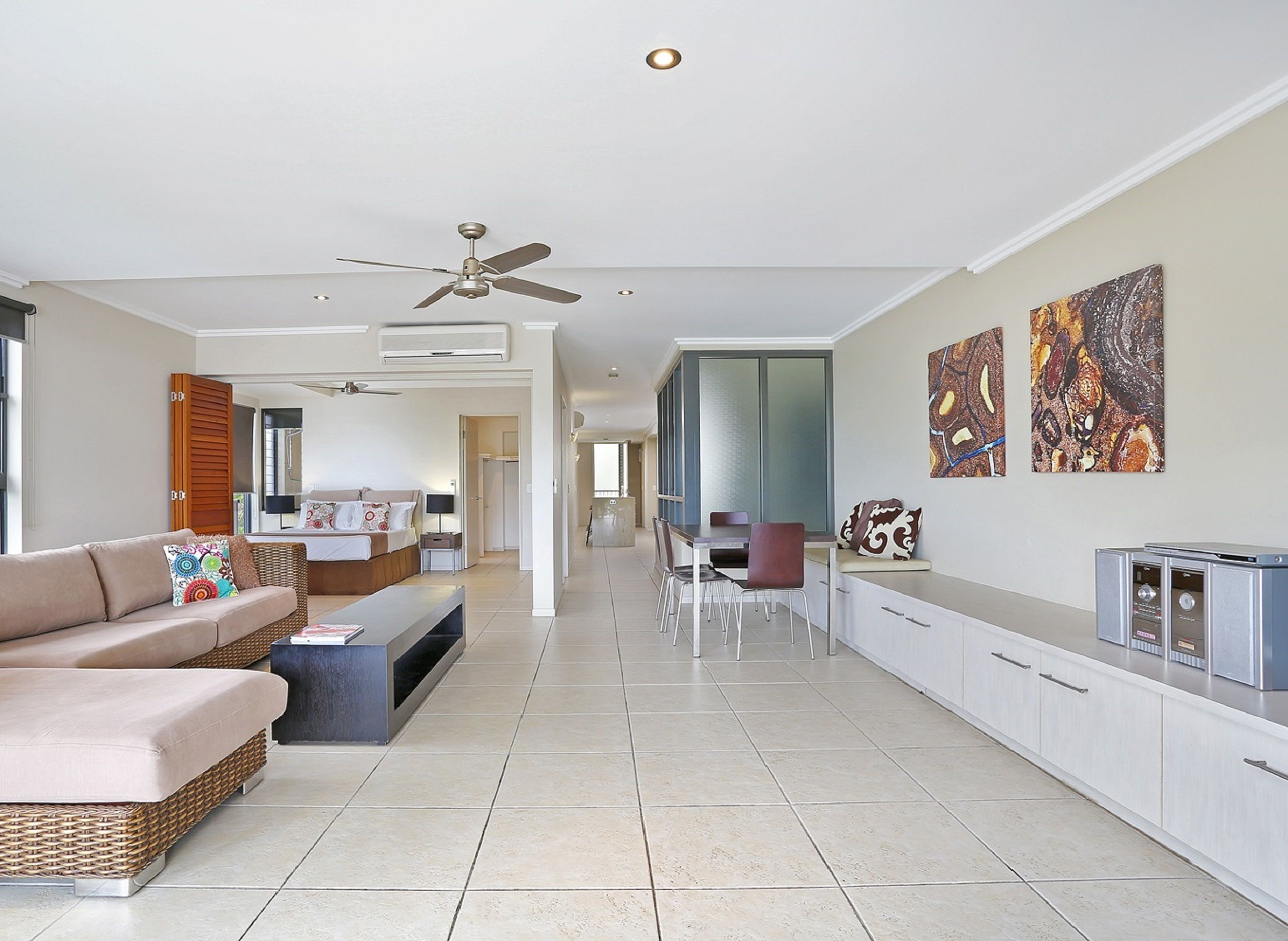 A spacious living area with a sofa, a dining table, and chairs. There is a ceiling fan and a TV on a cabinet.