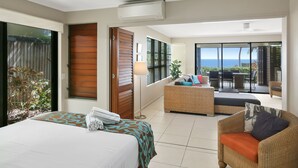 Une chambre d’hôtel avec un lit, un canapé en osier et un balcon donnant sur l’océan.