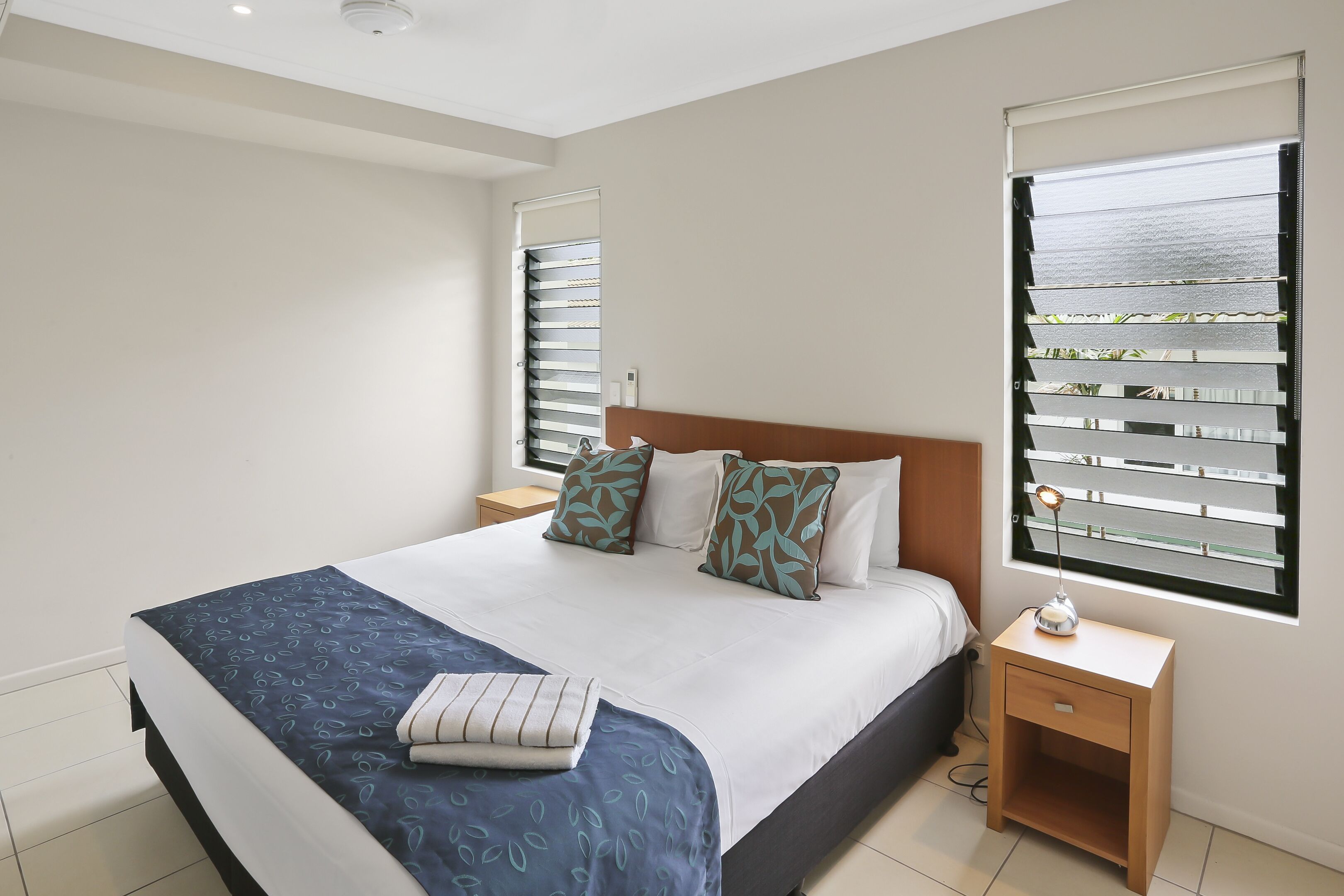 A bedroom with a bed, nightstands, a lamp, and a window with blinds.